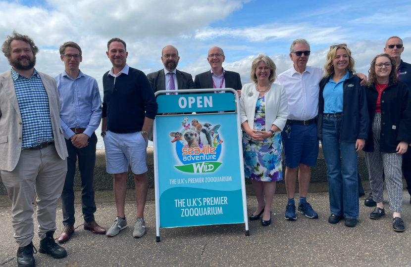 In a floral blue and white summery frock, Anna Firth MP stands with her fellow Southend MP Sir James Duddridge and a number of other men on Southend's seafront